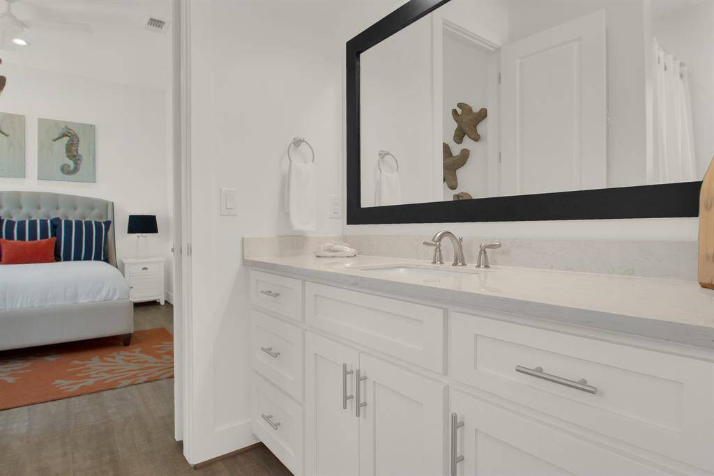 A large mirror extends over the sinks. The adjoining bedroom hints at a cozy, colorful design.