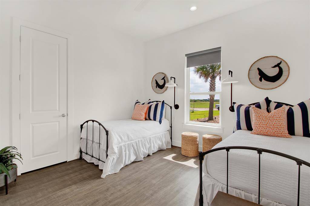 This is a bright, well-lit bedroom with two twin beds, featuring a clean, modern design, and ample natural light from a window with a view of greenery, and a neutral color palette.