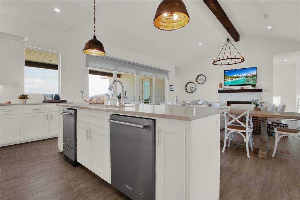 The open-plan kitchen features a central island with an ice maker, an undermount sink and stylish pendant lighting. The space seamlessly flows into a dining area, illuminated by natural light.