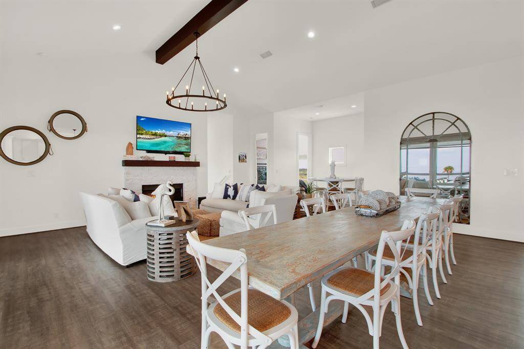 The living and dining space merge with modern finishes, featuring enough space for a large dining table (as shown here), comfortable seating area, and a cozy fireplace. Natural light streams in through the window, offering a view of the outside.