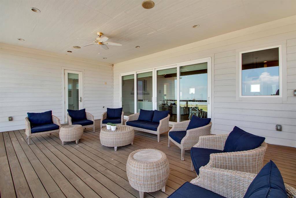 This is a spacious, covered outdoor deck area on the second level of the home offers a ceiling fan for warm days, and easy access to the interior through sliding glass doors. The wooden flooring and white siding create a classic, coastal vibe. Perfect for relaxation and entertaining.