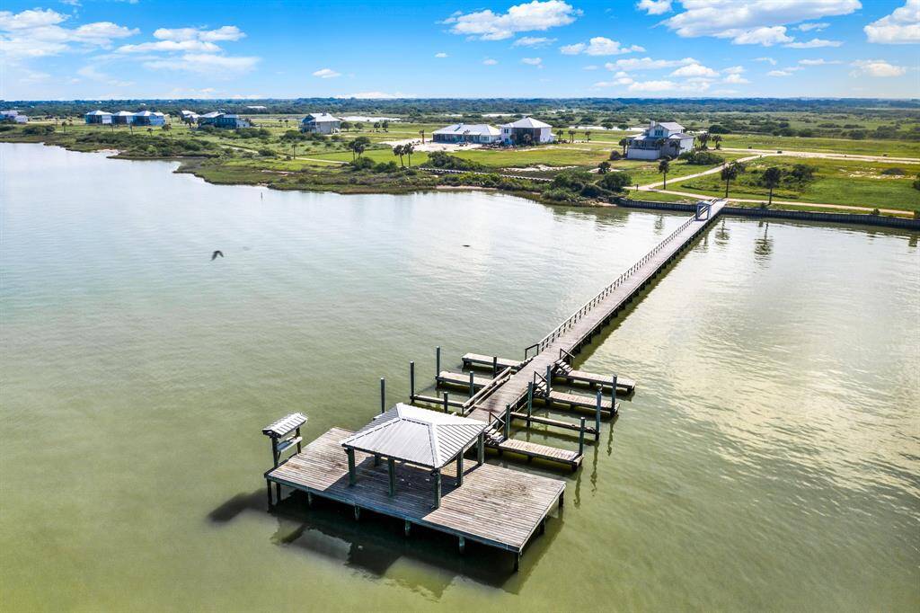 This property offers a public pier extending into a serene body of water, offering direct access for boating or fishing. The surrounding landscape includes open green spaces and a few scattered homes, suggesting a peaceful, rural setting with expansive views.