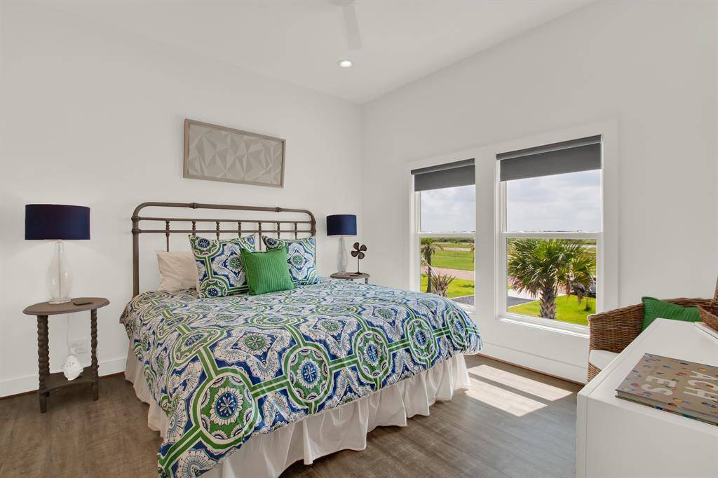 This is a bright and inviting bedroom on the second floor with its own en suite bathroom.  It features a queen bed,  two windows offering natural light and views of the outdoors and a ceiling fan for comfort.  The room has a clean, modern aesthetic with ample space for personalization.