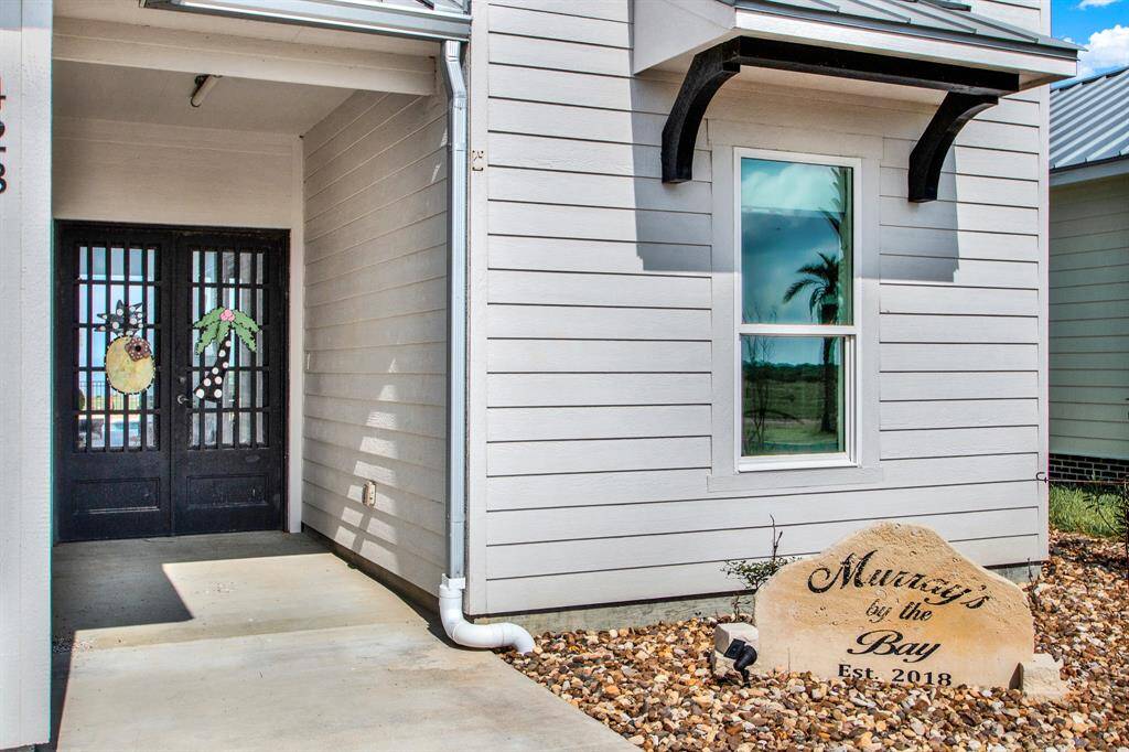 This welcoming entryway features a modern front door with glass elements set in a clean-lined exterior with light siding. A personalized decorative stone adds a charming touch to the landscaping.