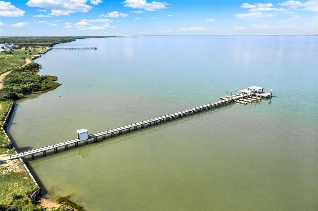 The serene waterfront property with a long pier extending into a calm bay, featuring a covered seating area at the end, perfect for enjoying the expansive water views.