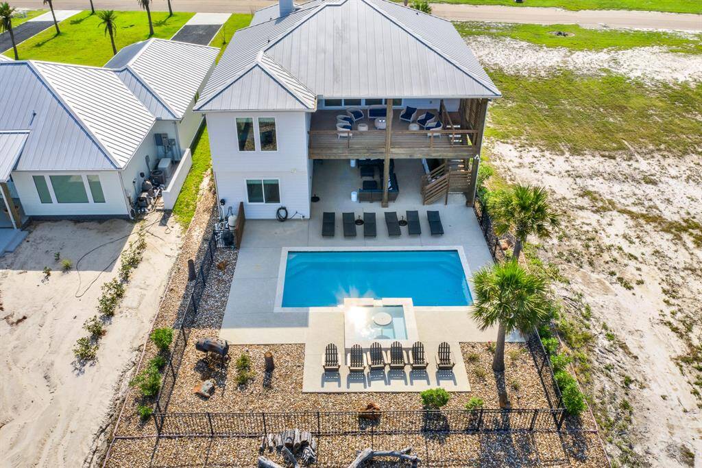 The aerial view of the home featuring a showing the area with the pool, lounging chairs, and a covered patio, all surrounded by a landscaped yard with palm trees, and located near the boat dock and areas for fishing all around.