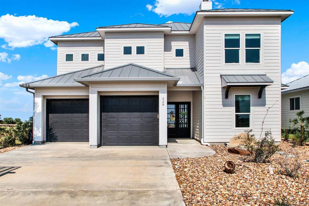 This is a modern two-story home features a light gray exterior with white trim and a dark gray roof. It includes a two-car garage, a covered entrance, and a low-maintenance landscaped front yard.