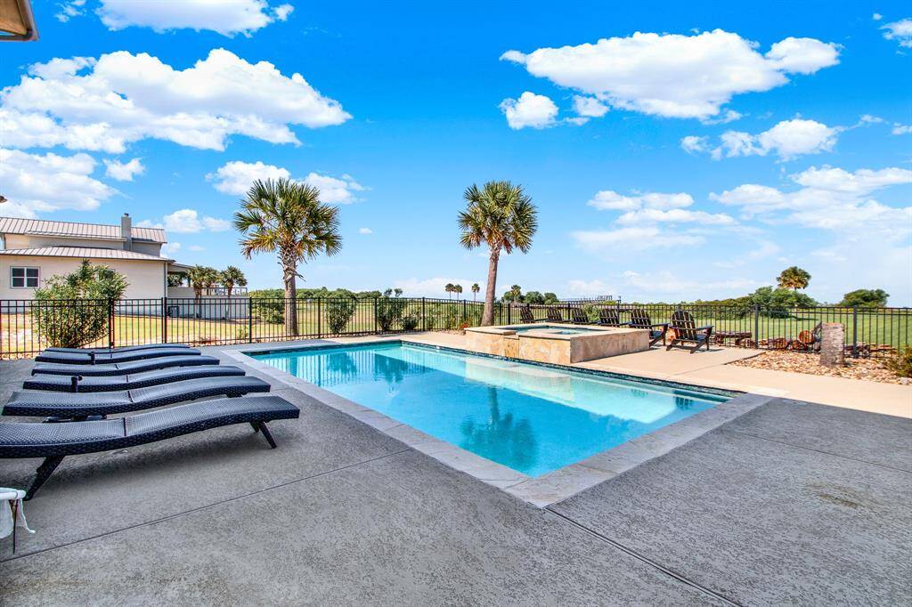 A beautiful outdoor pool area with a clear blue sky and a spacious deck with lounge chairs, showcasing a relaxed lifestyle with a view of an open landscape beyond the fenced perimeter. Perfect for leisure and entertainment.