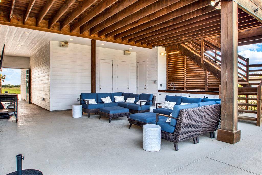 A spacious covered patio with comfortable outdoor seating, perfect for relaxation and entertaining. The area is well-sheltered by a wooden beam ceiling, and the white-paneled wall adds a touch of modern charm charm.