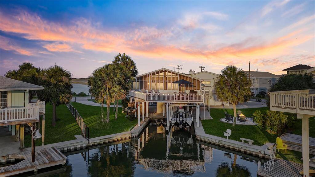 This waterfront home features a spacious outdoor deck overlooking a canal, complete with a private boat dock and lift. Surrounded by lush greenery and palm trees, it offers a serene sunset view, perfect for coastal living.