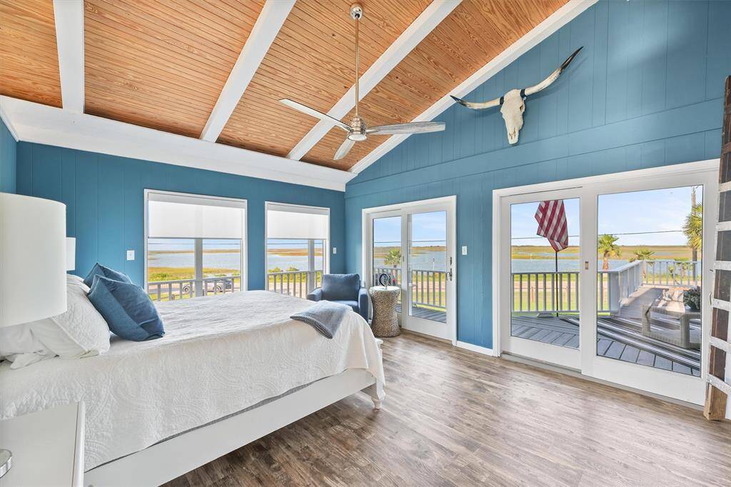 This bright, airy bedroom features a vaulted wood ceiling and large windows with stunning waterfront views. It includes sliding glass doors leading to a spacious deck, perfect for enjoying the scenery.