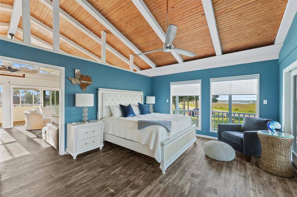 Bright and airy 2nd Primary bedroom with vaulted wooden ceiling and large windows offering scenic views. Features a en-suite,  cozy seating area, loft, modern fan, and easy access to a sunlit sitting area. Ideal for relaxation and enjoying the outdoors.