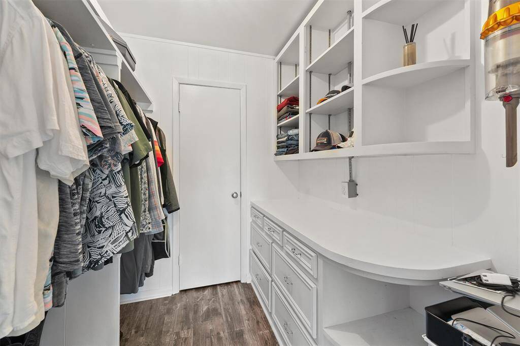 This photo showcases a spacious walk-in closet with ample shelving, hanging space, and drawers. The closet features clean white cabinetry and dark wood flooring, offering a well-organized and stylish storage solution.