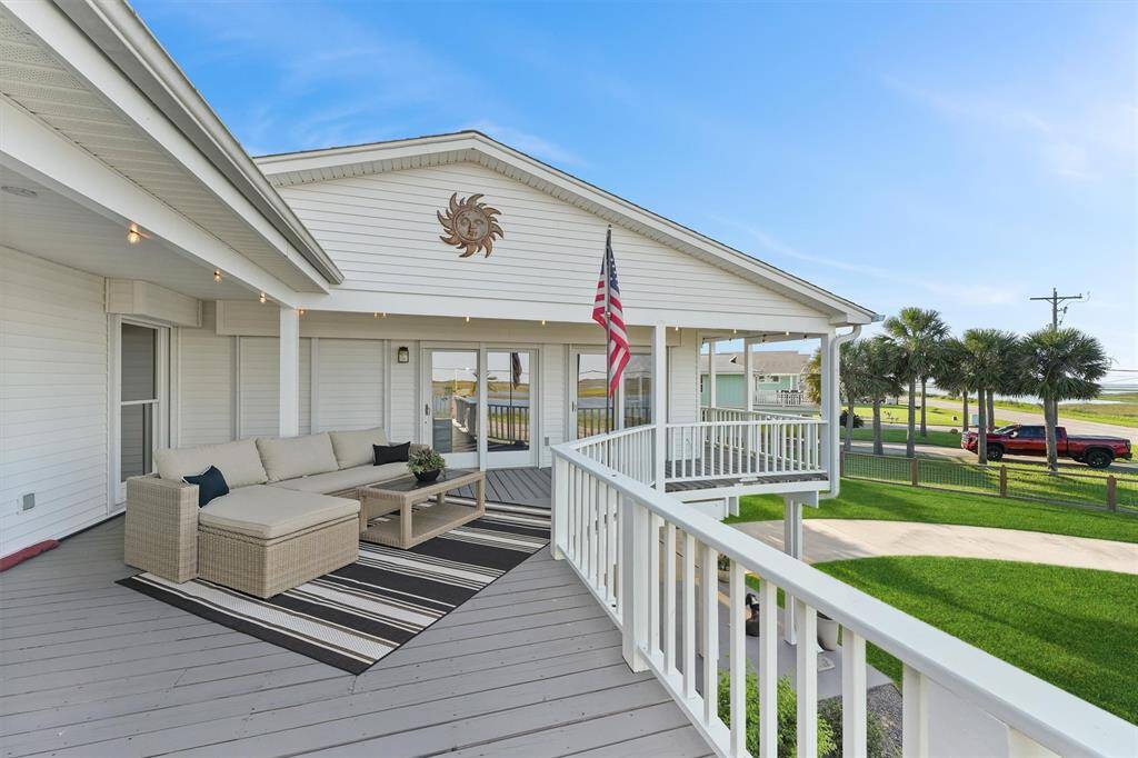 This inviting home features a spacious deck with comfortable seating, perfect for outdoor relaxation. The area is well-maintained with a view of palms trees and easy access to the bay across the street, ideal for enjoying sunny days.