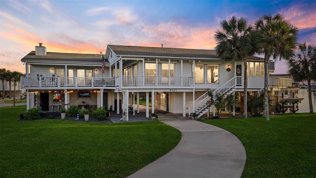 This beautiful waterfront home features a spacious two-story design with expansive balconies, a lush green lawn, and stunning sunset views. The exterior boasts a modern yet cozy style, perfect for enjoying outdoor living.