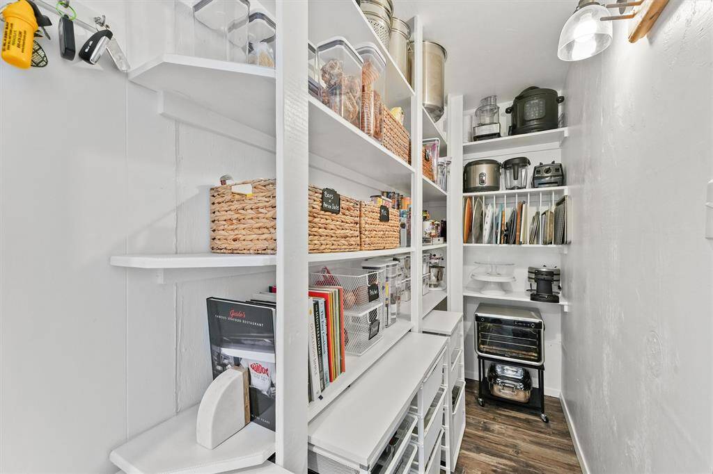 This photo showcases a well-organized pantry with built-in shelves, ample storage baskets, and clear containers for easy access. It features a variety of kitchen appliances neatly arranged, making efficient use of space. The room has a clean, bright aesthetic with a modern light fixture.