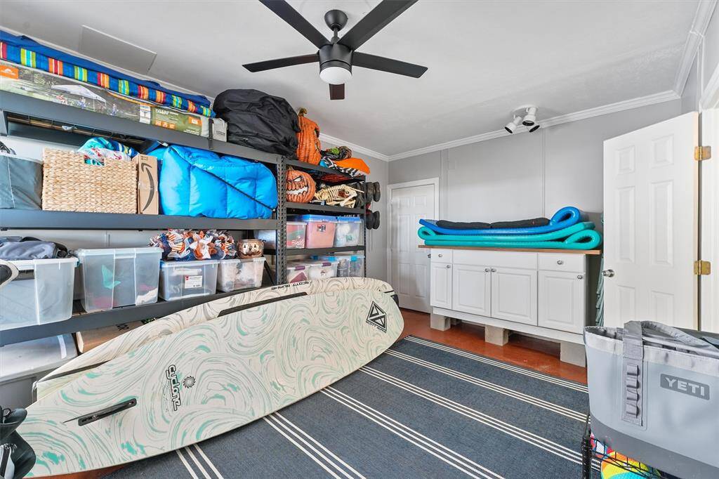 This room is a well-organized storage space featuring wall shelves loaded with bins and equipment, a ceiling fan, and a cabinet for additional storage. It’s ideal for organizing sports gear or outdoor equipment.   This could make a perfect spot for a 4th bedroom.