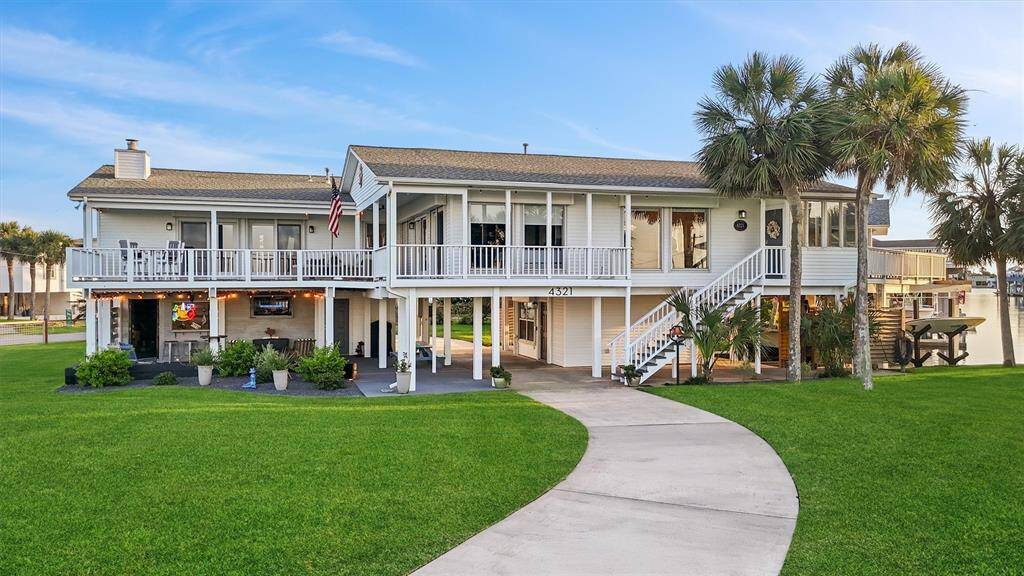 This elevated waterfront home features a spacious balcony, lush green lawn, and outdoor entertaining area. It offers a scenic view with palm trees and easy access to water. Perfect for those seeking a coastal lifestyle.