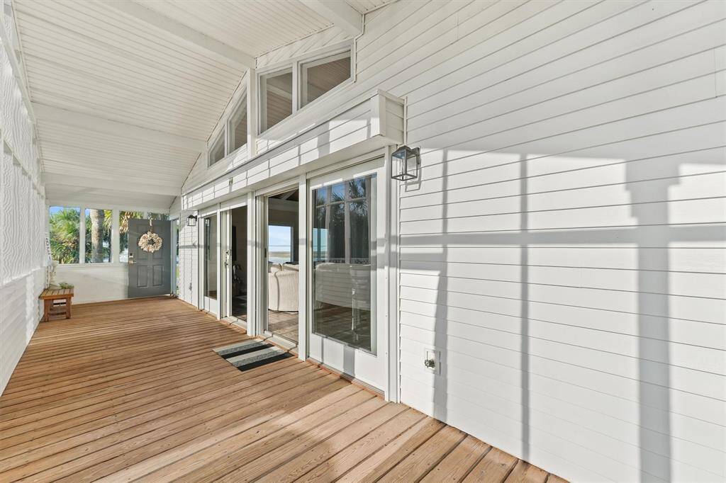 Bright and airy enclosed porch with high ceilings, wooden flooring, and ample natural light. Features sliding glass doors opening to the interior and views of the canal. Ideal for relaxation and entertaining.