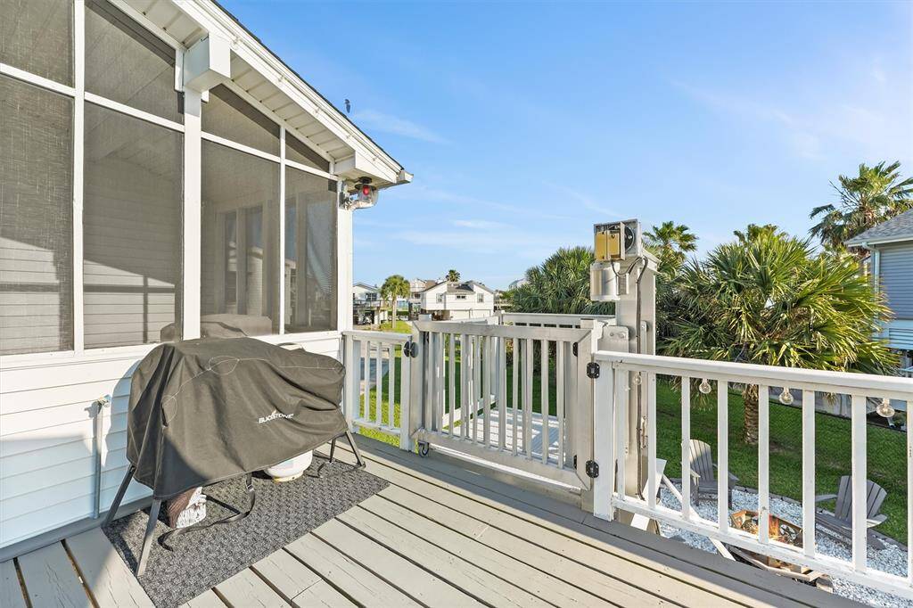 Charming deck with a grill, screened porch, and views of a lush backyard featuring palm trees and a cozy fire pit area all overlooking the Canal. Ideal for outdoor entertaining.
