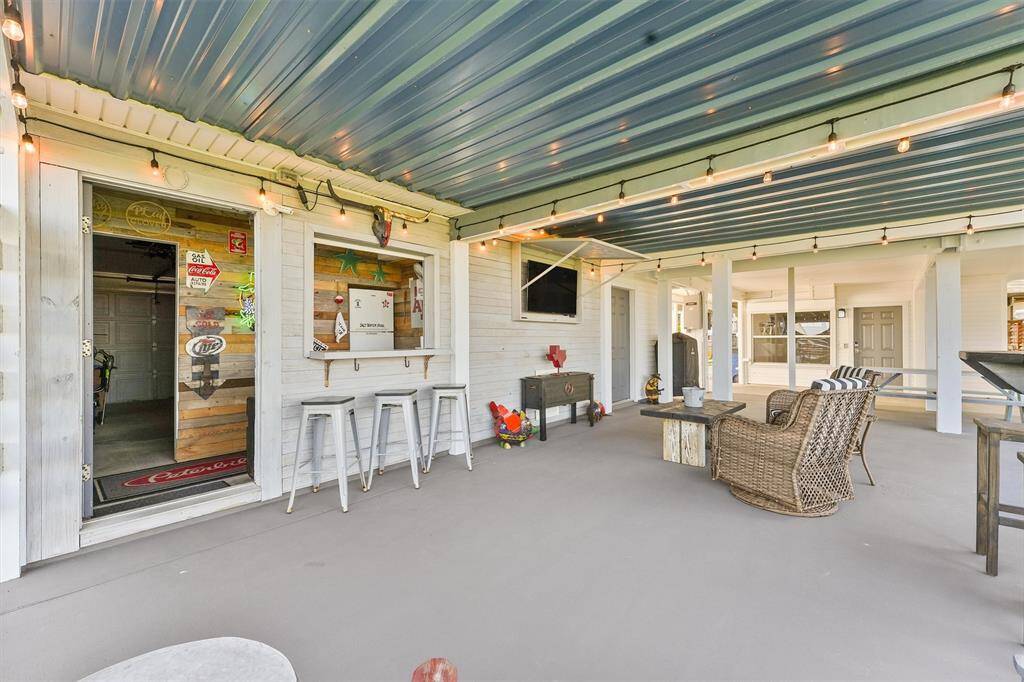 This photo showcases a spacious covered patio with a cozy seating area and a bar setup. The area features a string of lights for ambiance and a TV mounted on the wall, perfect for outdoor entertainment and relaxation.