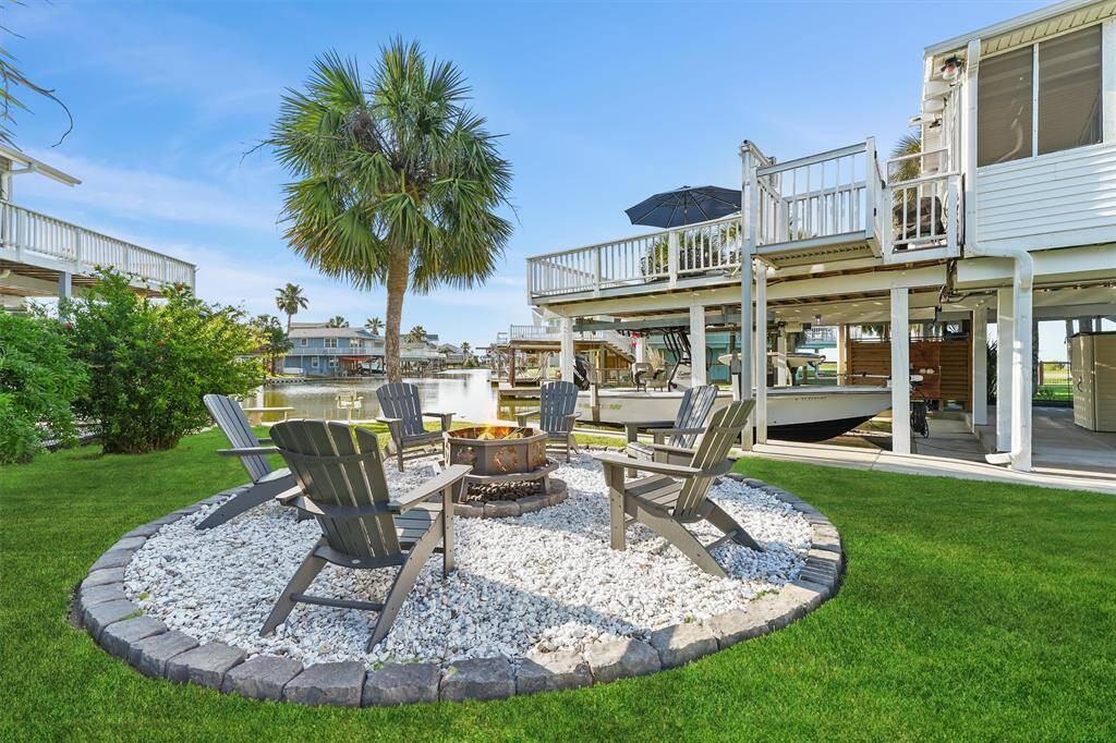 Charming waterfront property with a cozy outdoor fire pit area, featuring Adirondack chairs on a stone patio with fire pit surrounded by lush green grass. The house includes a boat dock, providing easy water access and picturesque views. Perfect for relaxation and entertaining.