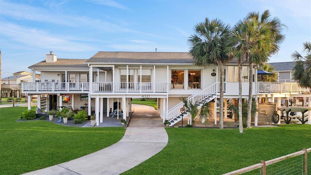 This charming coastal home features a raised design with a spacious deck, surrounded by lush green lawns and tropical palm trees. It offers a blend of outdoor and indoor living, ideal for relaxation and entertaining.