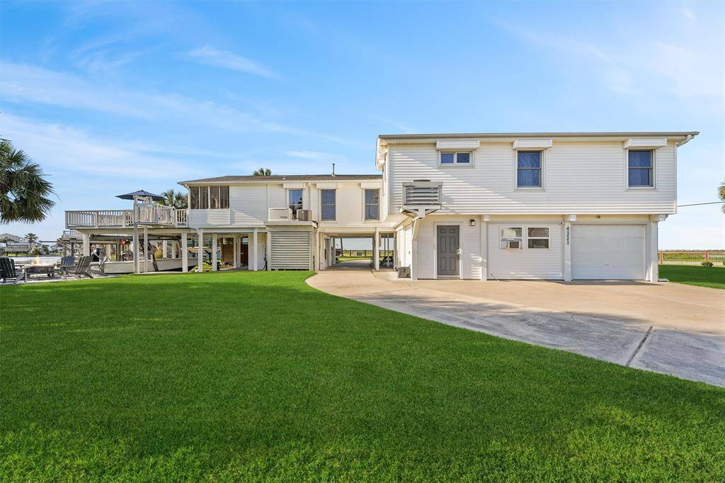 This photo features a spacious two-story home with a large, well-maintained lawn. The exterior is light-colored, and there's a substantial driveway leading to a garage. The house has an elevated deck, perfect for outdoor relaxation and entertaining.