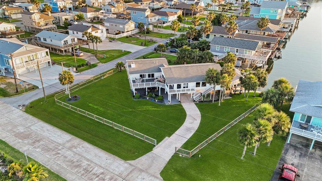 This photo showcases a spacious waterfront home with a large, well-maintained lawn, surrounded by palm trees. The house features a wraparound porch and a driveway leading to a detached garage. It's situated in a charming neighborhood with canal access, ideal for boating enthusiasts.