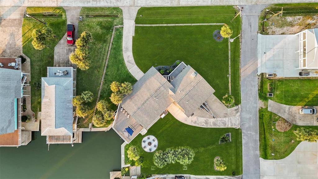 This aerial view shows a waterfront home with a large, neatly landscaped yard and driveway. The property is adjacent to a canal, ideal for boating or water activities. The neighborhood appears peaceful and well-maintained.