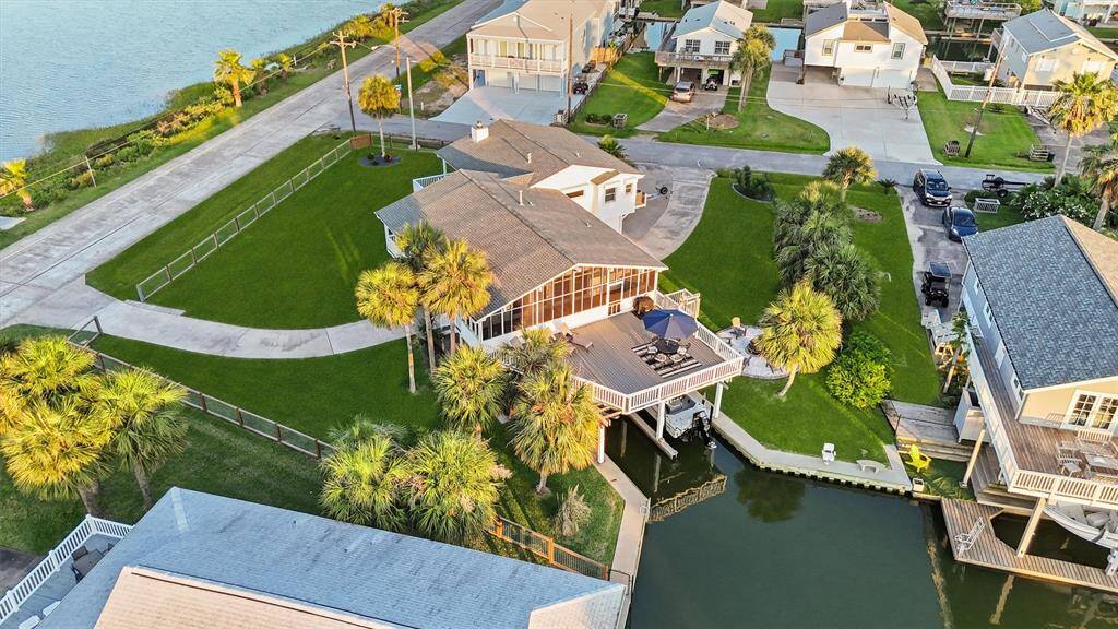 This aerial view showcases a charming waterfront home with a spacious deck, surrounded by lush green lawns and palm trees. It features direct canal access, perfect for boating enthusiasts, and is located in a serene neighborhood, offering a blend of privacy and scenic views.