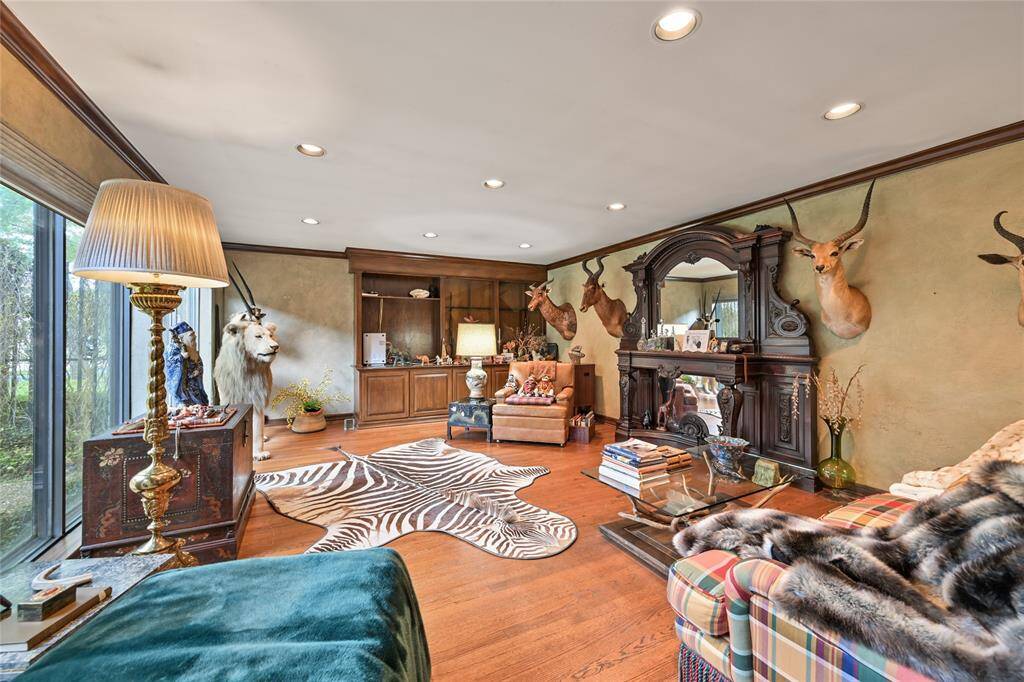 A cozy yet grand den featuring rich wood flooring, custom built-ins, and a striking antique fireplace surround—perfect for entertaining or relaxing in style.