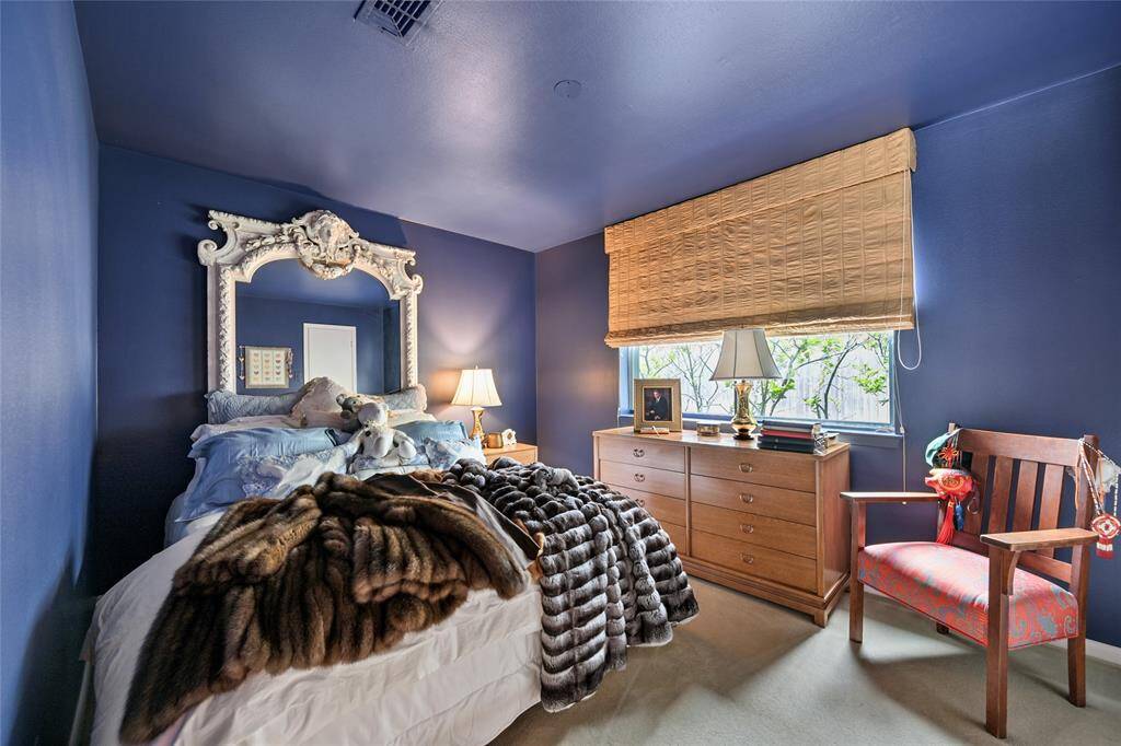 A charming guest suite with a dramatic color palette, regal headboard, and natural light filtering through roman shades—perfect for a restful escape.