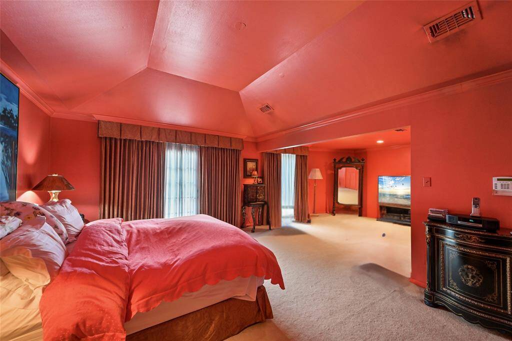 This expansive primary suite features dramatic tray ceilings, rich coral tones, and a generous sitting area that offers flexible space for relaxation or entertainment.