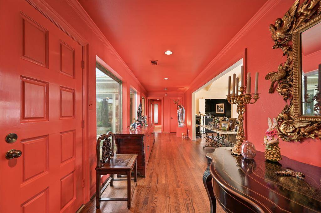 This bold coral-toned hallway with hardwood floors, gallery-style lighting, and expansive windows overlooking the interior courtyard makes for an unforgettable first impression.