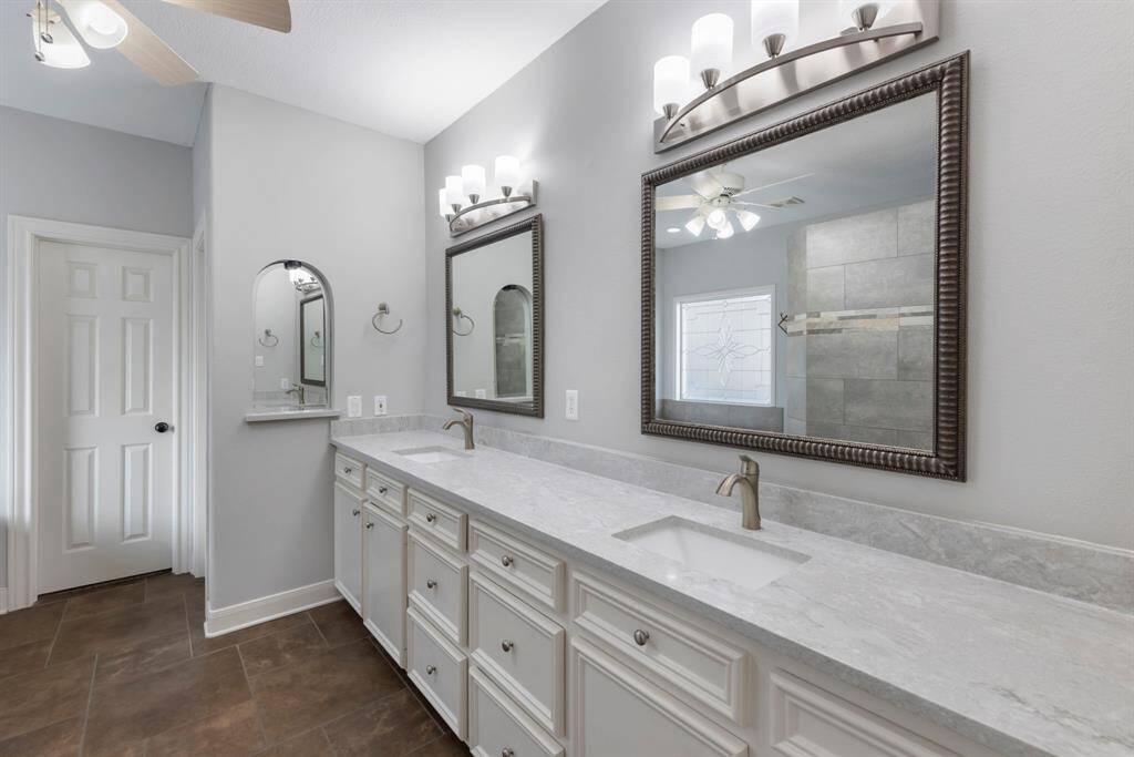 The primary bathroom, featuring dual sinks and gleaming quartz countertops. The expansive mirrors reflect the beauty of the modern fixtures, inviting you to start and end your day in style and comfort.