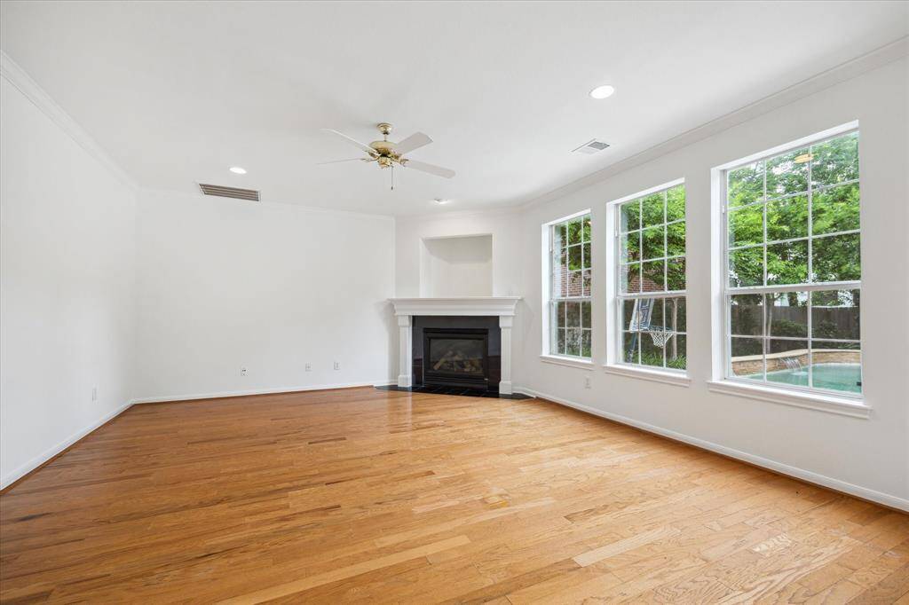 Bright and spacious family room with hardwood floors, a cozy fireplace, and large windows offering plenty of natural light and views of the backyard pool.