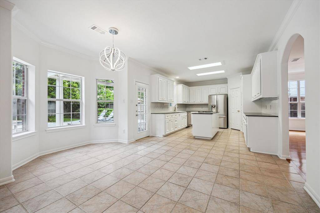 This bright kitchen features white cabinetry, a central island, and excellent storage. Large windows provide ample natural light, and the tiled floor adds a touch of elegance. An open layout connects seamlessly to adjacent spaces.