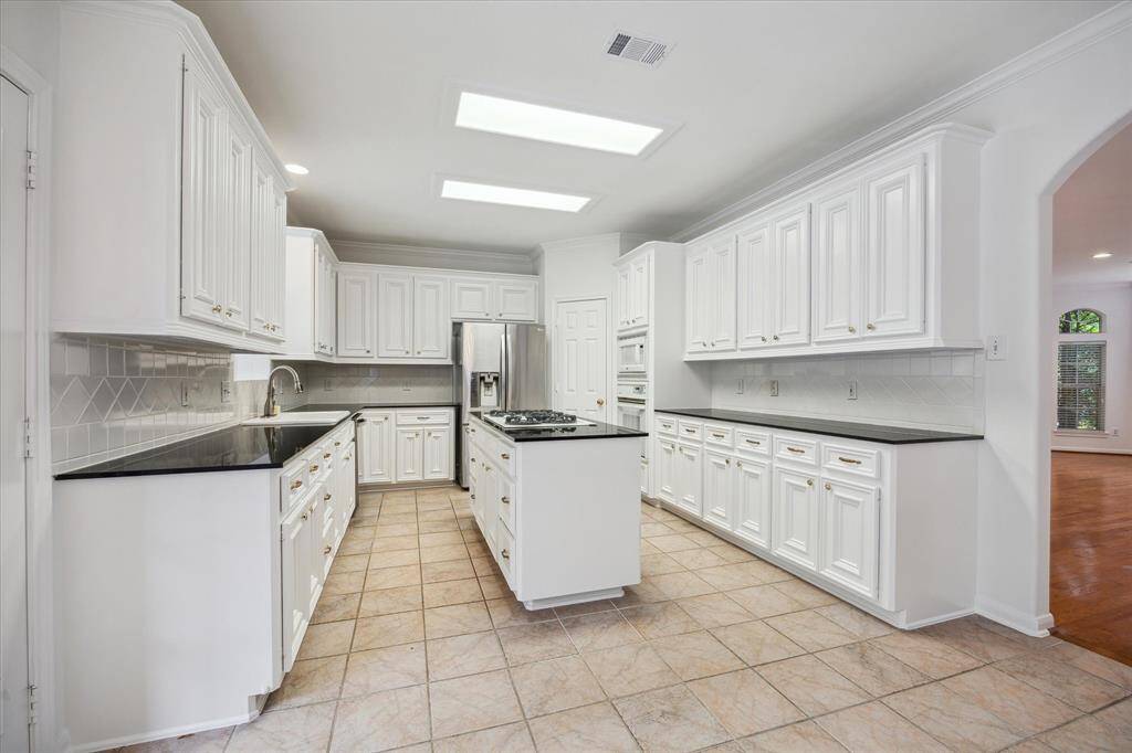 This spacious kitchen features sleek black countertops, ample white cabinetry, and a central island with a cooktop.