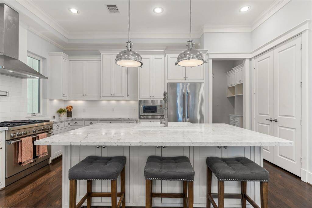 This kitchen is a chef’s delight, with elegant cabinetry, hardwood floors, a large island/breakfast bar, stainless steel appliances, and stone countertops, all highlighted by recessed lighting and crown moldingThis stunning kitchen is a dream for any chef, featuring elegant cabinetry, gleaming hardwood floors, a spacious island/breakfast bar, stainless steel appliances, and stone countertops, all beautifully accentuated by recessed lighting and refin