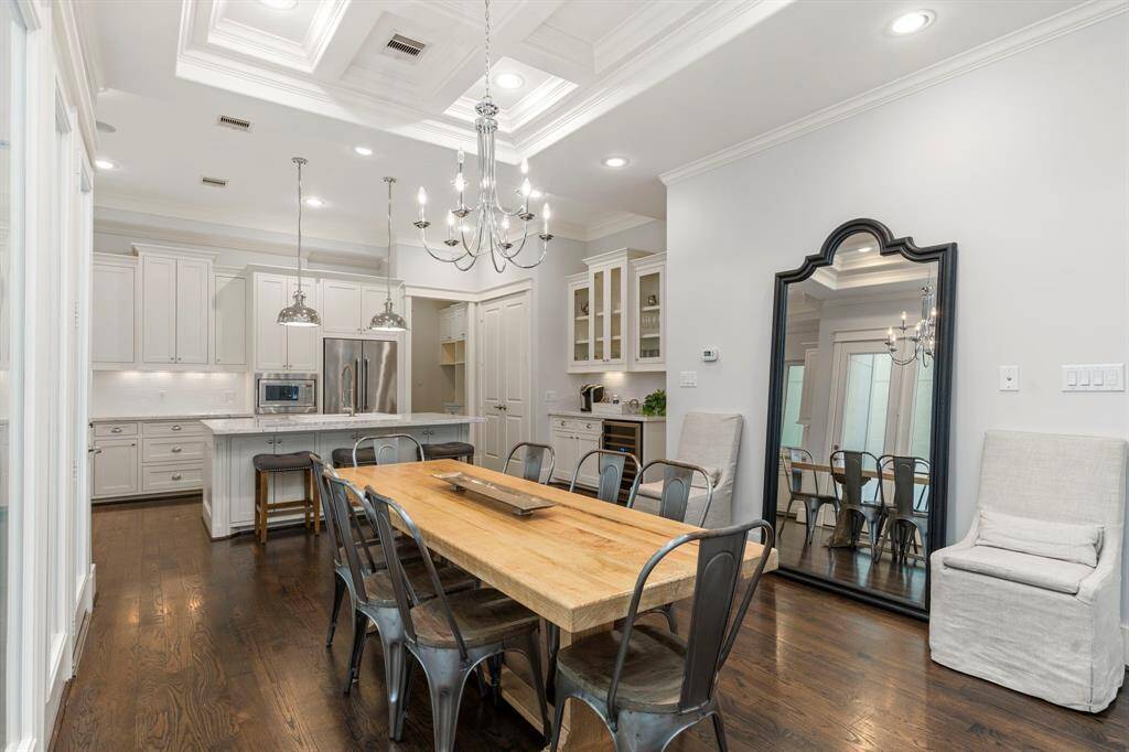 The dining area, located just off the kitchen, offers a striking coffered ceiling and a graceful chandelier, paired with gleaming hardwood floors and a wall of windows that flood the space with natural light.