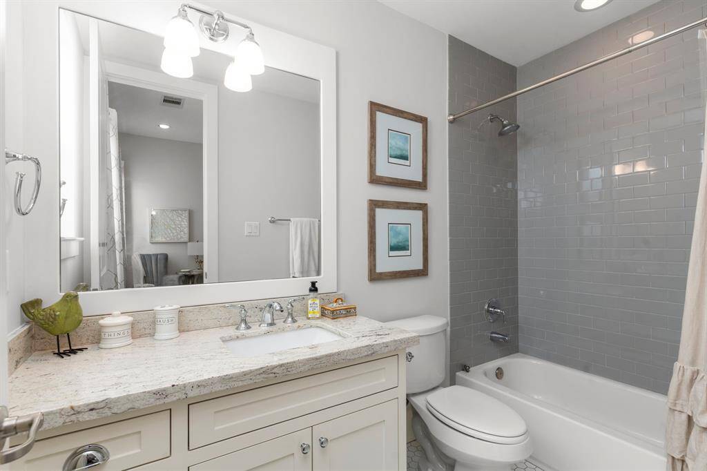This elegant ensuite bathroom features a granite slab countertop, white cabinetry, and a tub/shower combination with stylish gray subway tiles extending to the ceiling.