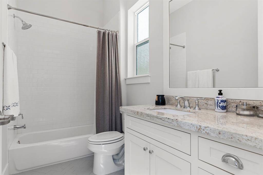This bright and airy ensuite bathroom offers a granite countertop and a tub/shower combination, beautifully accented by a subway tile wall.
