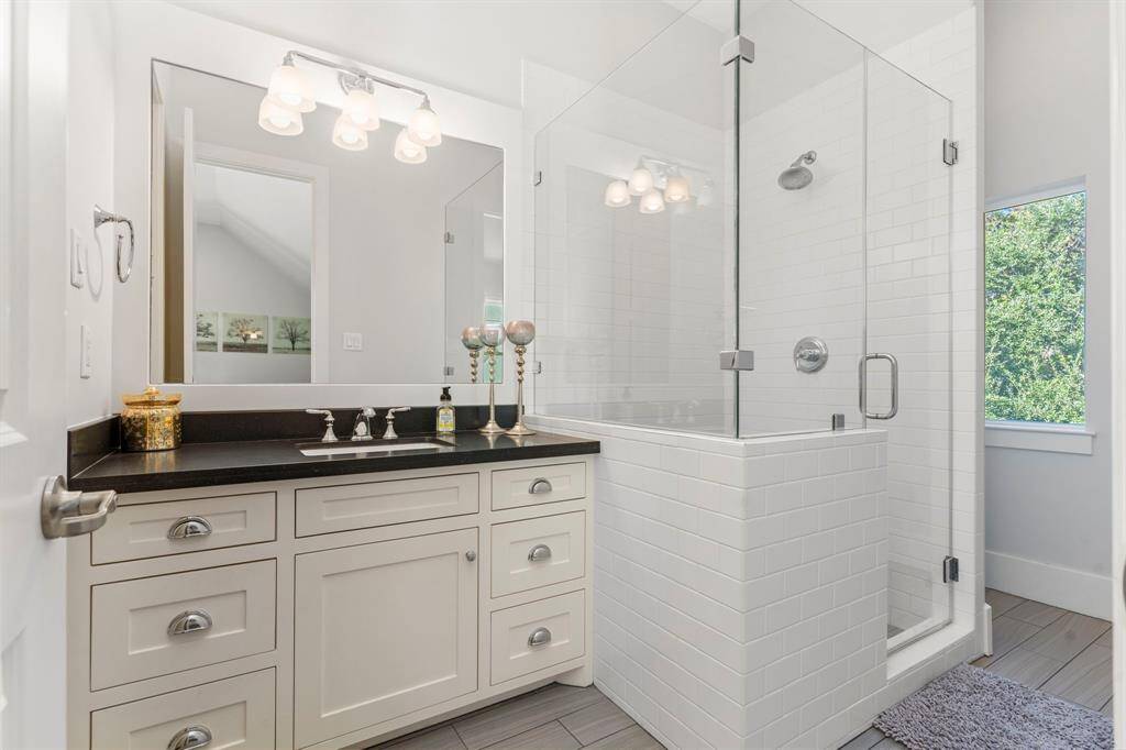 This elegant ensuite bathroom features a granite countertop, framed mirror, white cabinetry, stylish tile flooring, and a walk-in shower accented with crisp white subway tiles.