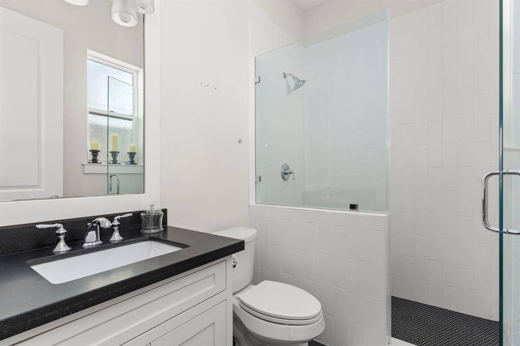 The ensuite bathroom features granite slab countertops and dark tile floors, creating a striking contrast against the white walls and the subway-tiled glass shower.