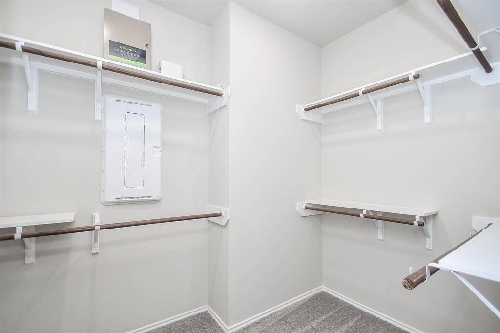 This photo showcases a spacious walk-in closet with multiple wooden rods for hanging clothes and several shelves for storage, all set against neutral-colored walls and carpeted flooring.