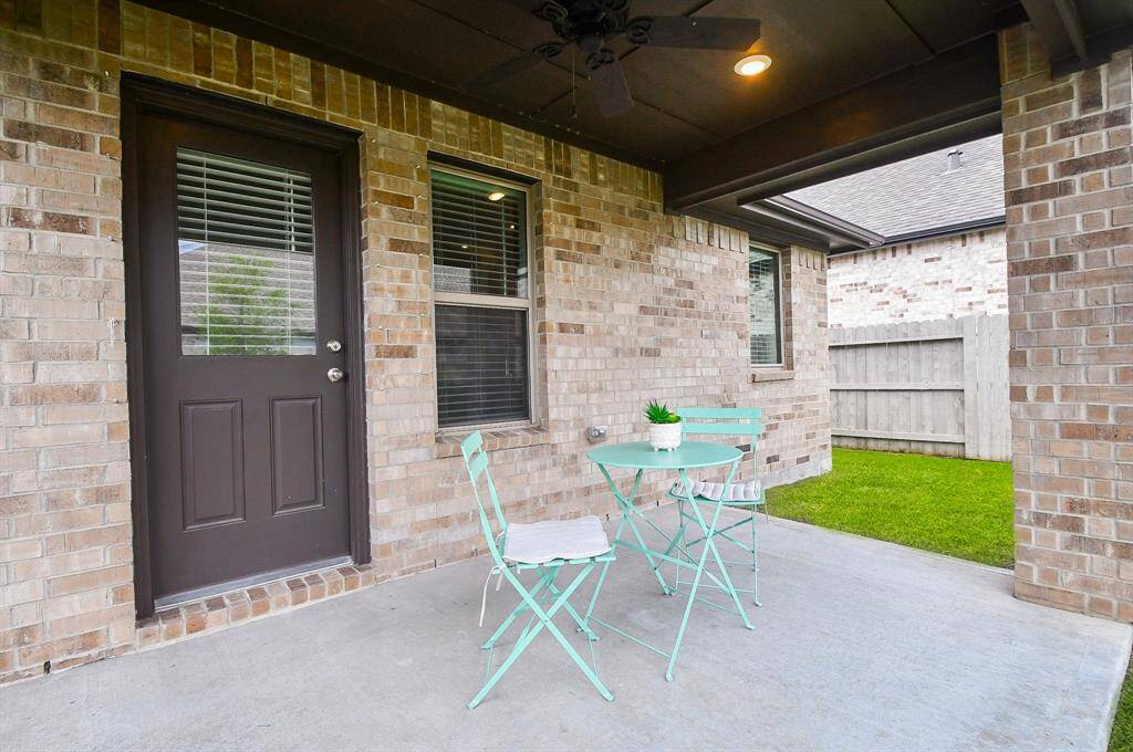 This photo showcases a cozy covered patio with brick walls and a small bistro set, perfect for outdoor relaxation. The space overlooks a grassy backyard, enclosed by a wooden fence, offering privacy and comfort.