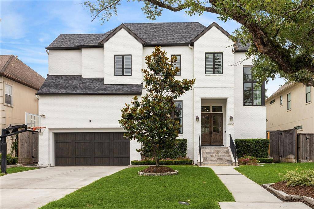 This stunning two-story residence in Bellaire showcases timeless curb appeal with its crisp white brick façade, rich dark wood accents, and contemporary black-trimmed windows. A manicured lawn, stately magnolia, and elegant stone entry staircase create a welcoming path to the grand double-door entrance.