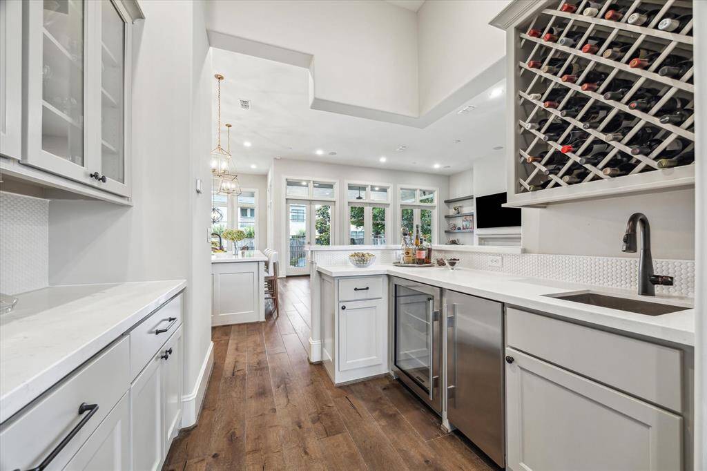 This elegantly designed butler’s pantry and wet bar seamlessly blend style and function, featuring crisp white cabinetry, a wine refrigerator, and built-in bottle storage that creates a striking visual display. Sleek quartz countertops, a textured backsplash, and rich hardwood flooring enhance the sophisticated ambiance, while the open sightline to the living and kitchen areas offers effortless flow for entertaining.