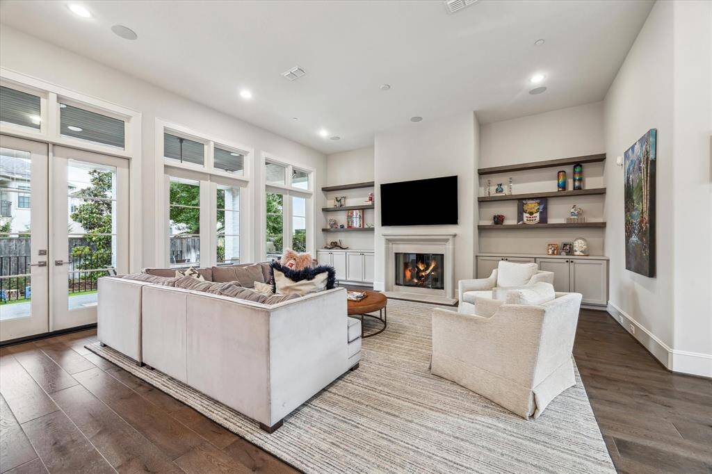 This inviting family room is anchored by a cozy gas fireplace framed in elegant molding and flanked by custom built-ins, creating a refined yet relaxed atmosphere. A wall of windows and French doors bathes the space in natural light while offering seamless access to the outdoor living area.